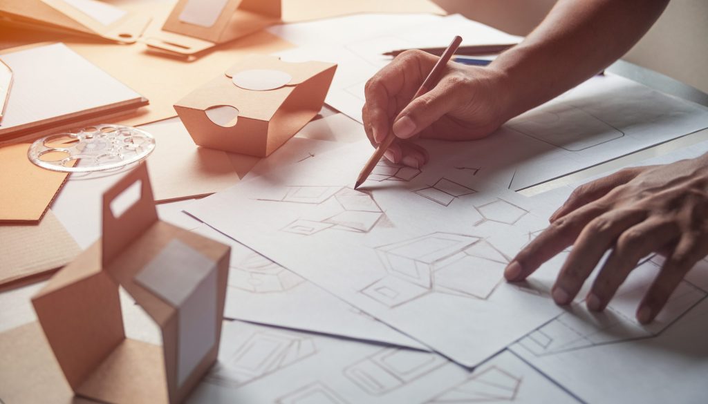 Persona che disegna modelli di design e forme tridimensionali su carta.